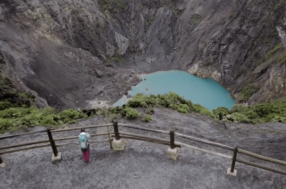 a woman geologist stands near the edge of a caldera of a volcano that currently has a basin of water