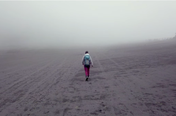 a woman with hiking gear walks in a barren misty landscape
