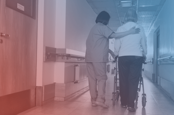 a nurse walks an elder woman using a walker down a hallway