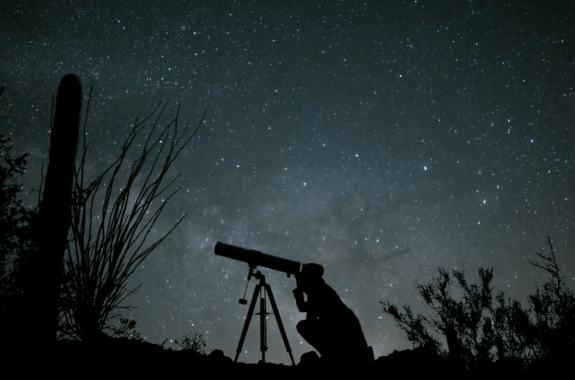 the shadow of a woman astrophysicist looking through a telescope in a desert landscape, with a beautiful starry backdrop