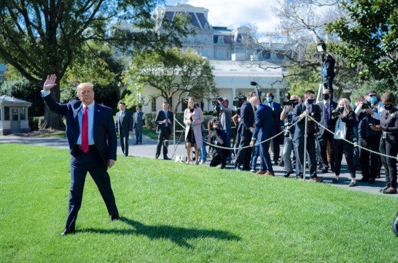trump walking on a lawn, waving at people and press