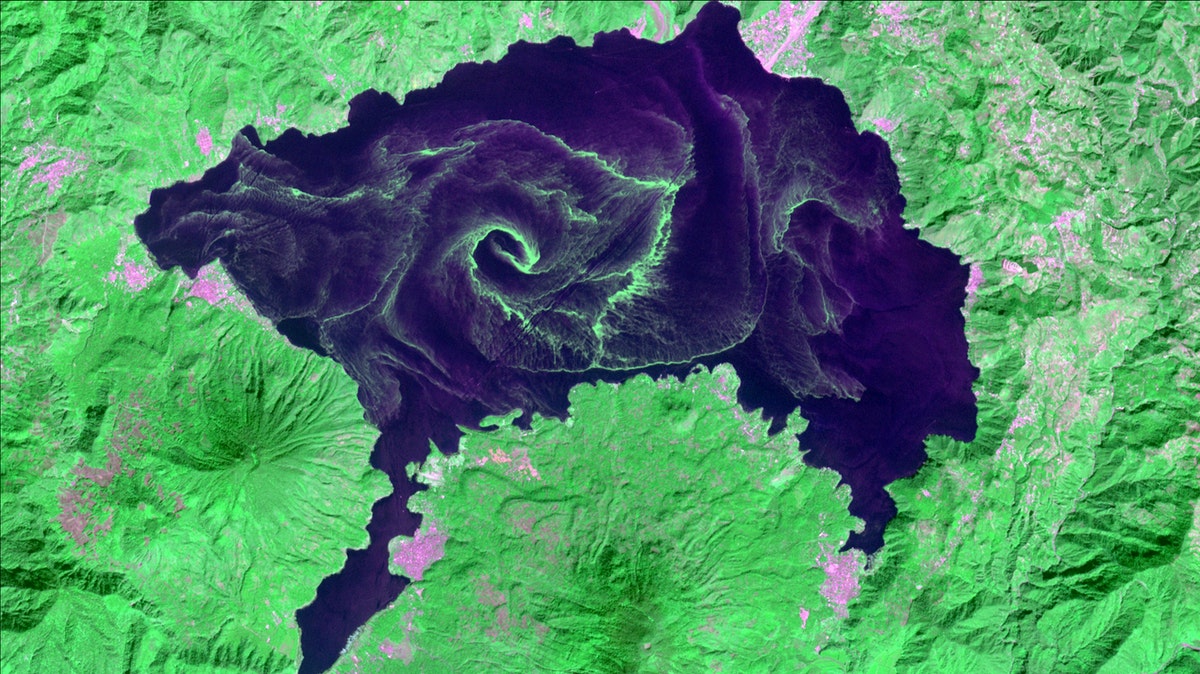 a satellite image of a lake that has large green swirls of algae in it
