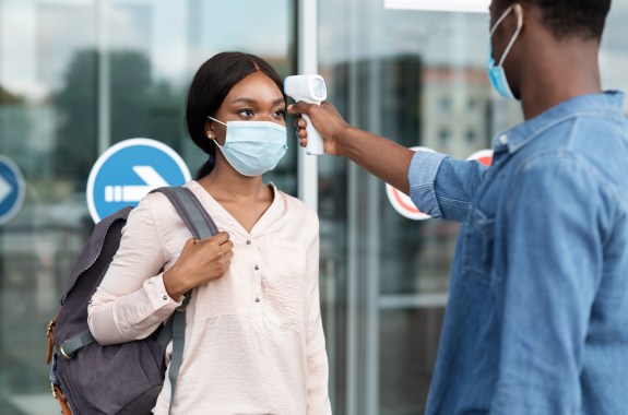 Airport Worker Checking Black Female Passenger's Temperature With Electronic Thermometer After Arrival, Covid-19 Outbreak Prevention