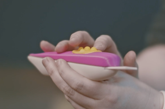 a person holds a bright pink pregnancy test stick that is larger and has a longer broader tip and textured surfaces that are easy to find and feel