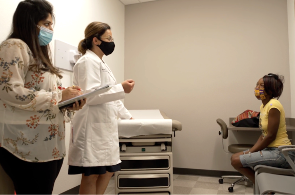 a female doctor and a female nurse wearing face masks debrief with a black woman patient in a face mask in a doctor's office