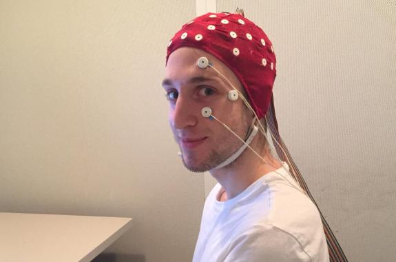 a man in a red beanie-like cap that has various electrodes on it to monitor brain signals