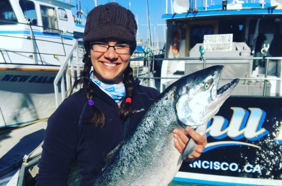 a woman in glasses and a beanie holds a large fish
