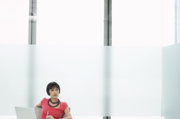 a woman thinking and staring off in the distance as she sits with a laptop in a modern cubicle office