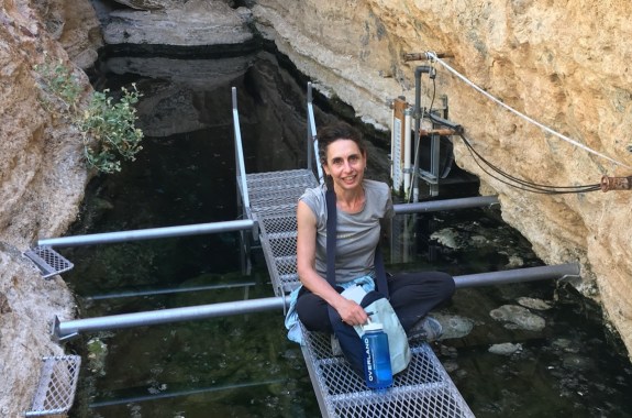 a woman sitting on narrow metal grated platforms over a waterway cutting through rock walls surrounding her