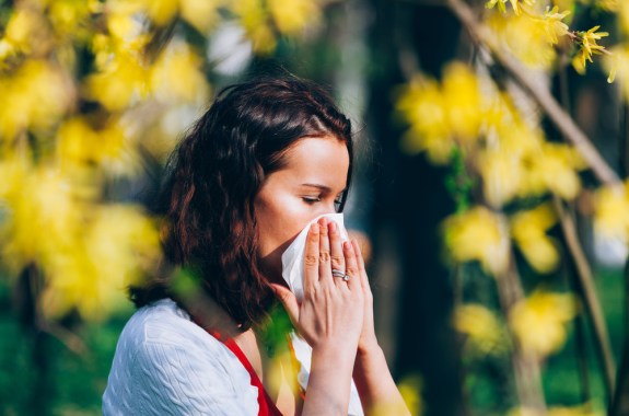 a woman outside sneezing into a tissue