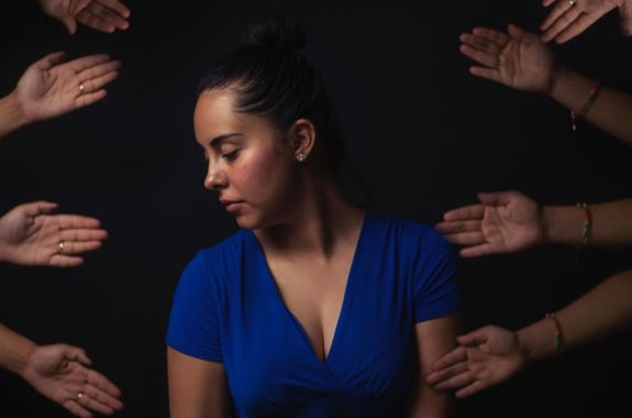 a woman with her eyes closed, head turned to the left. four pairs of hands are placed around her in an artistic fashion