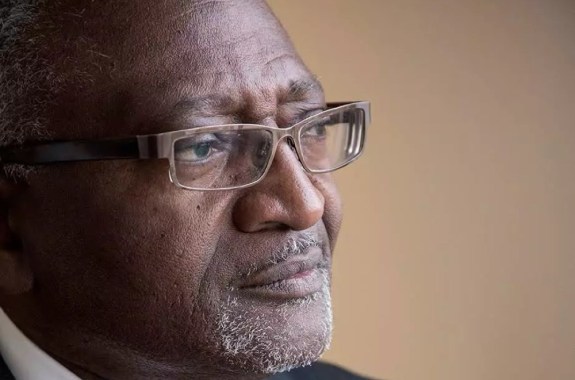 a profile headshot of a black man with glasses in a suit