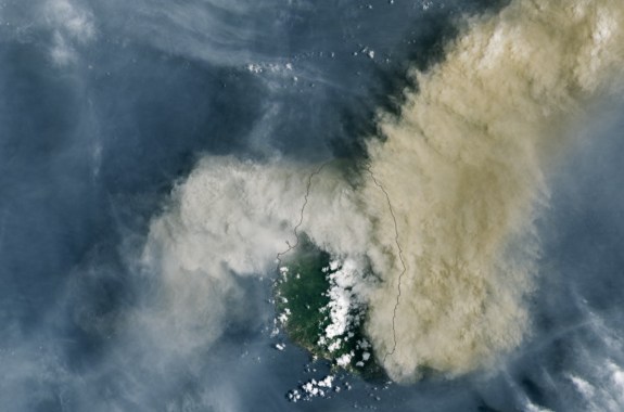 a satellite image of st vincent island, mostly shrouded by the plume of a volcano, drifting off to the right