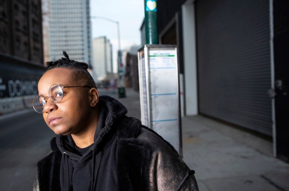 A transmasculine person waiting for the bus in a city close up