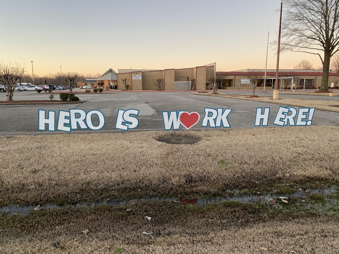 handmade large letters stuck in the grass outside a one story building that reads "heroes work here" with a heart replacing the 'o' in 'heroes'