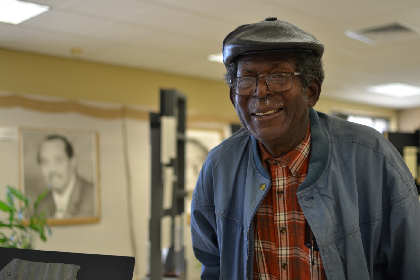 an older black man wearing a jacket and cap smiles at the camera