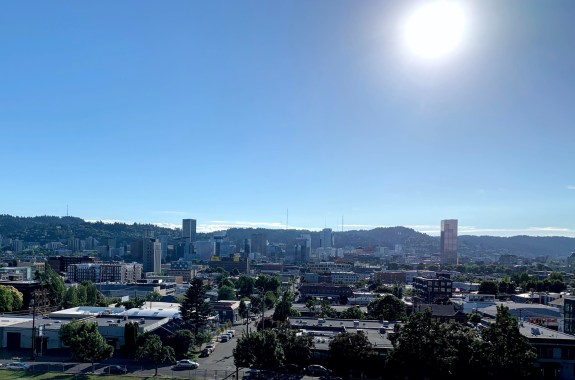 a clear hot day looking at downtown portland with mountains in the distance with the sun in frame