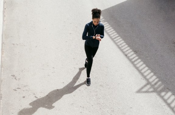 black woman walking outside in fitness clothing while checking her fitness tracker. its shot from above her