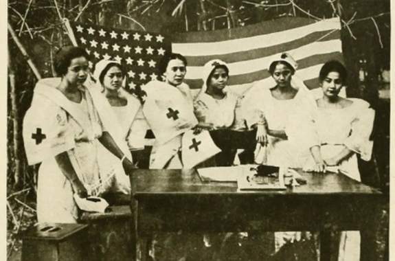 an old black and white photo of six filipino nurses in nurses uniforms standing behind a desk and in front of an american flag