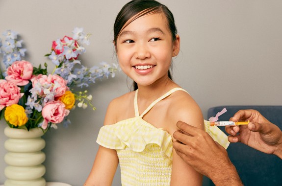 a young asian girl receiving a vaccine shot in her left arm. she's smiling.