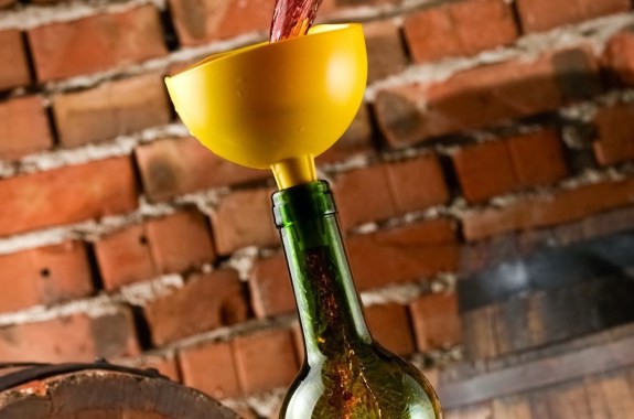 Pouring red wine in a bottle through a yellow funnel, against a background of bricks