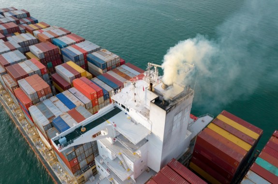 an aerial shot above a container ship loaded with containers on the ocean. its smoke stack emits smoke exhaust