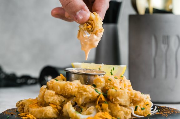 a person picking up a piece of calamari in sauce from a plate