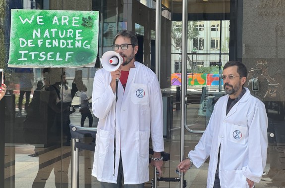 Two men chaining themselves to doors of a JPMorgan Chase & Co. Bank in Los Angeles. Behind them is a sign that reads: We are Nature Defending Itself