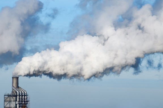 a factory with billowing smoke or gas coming out of a stack, filling up most of the image