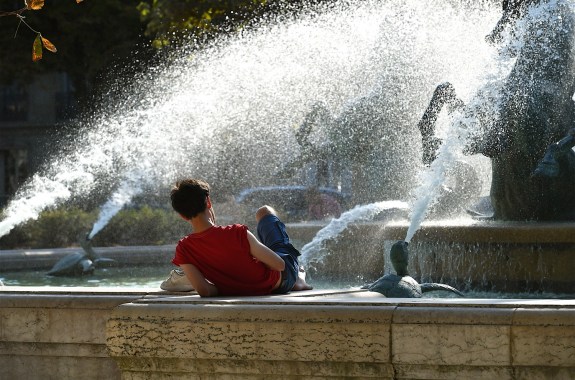 a young white man reading by a fountain during the hot weather in Paris France.