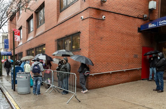 a group of people with umbrellas waiting in line in front of a hospital