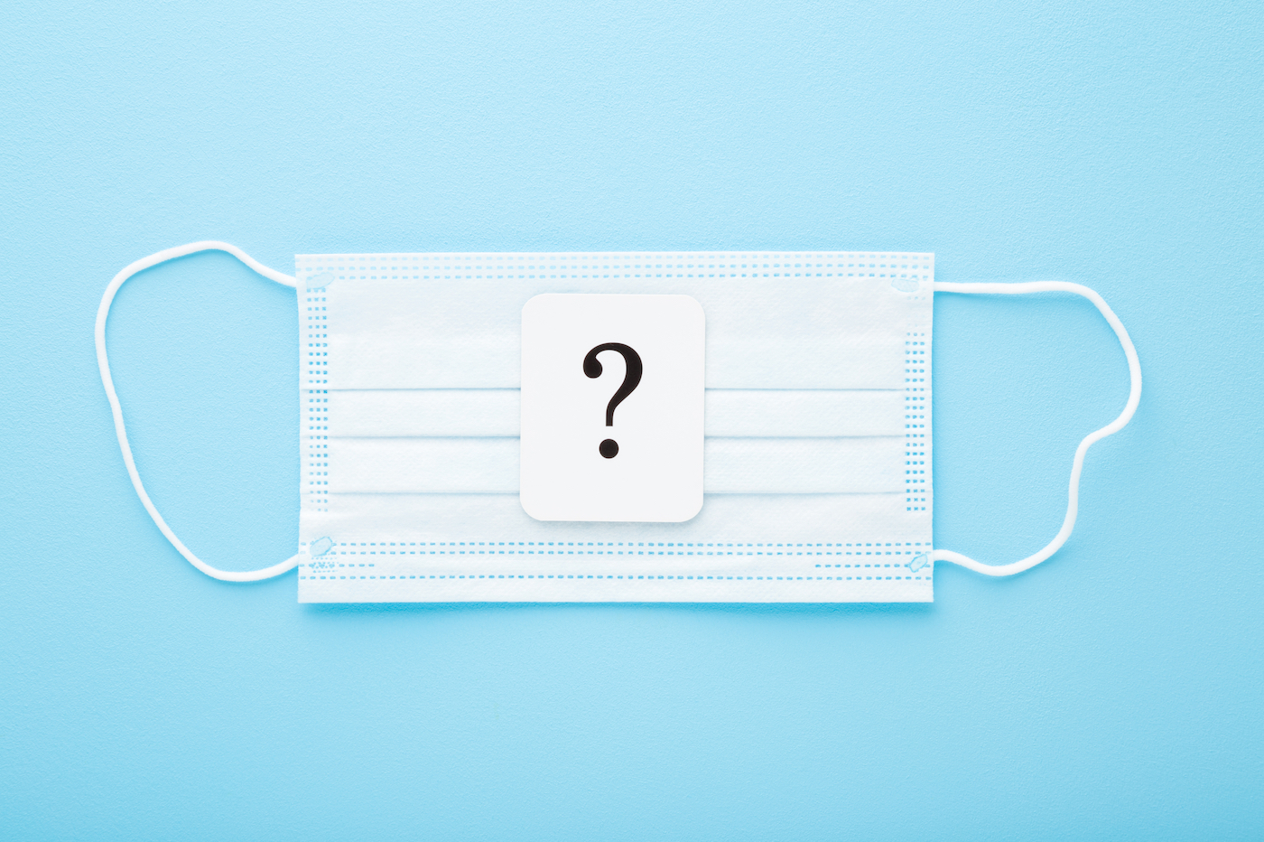 A small white card with a question mark on it rests on a blue surgical mask