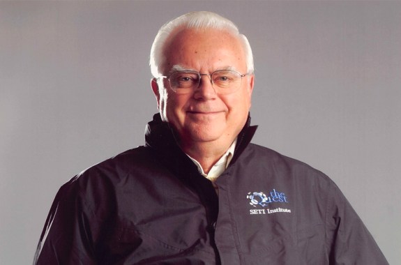 An older white man with glasses and a slight smile looking confidently at the camera, with a simple light gray background.
