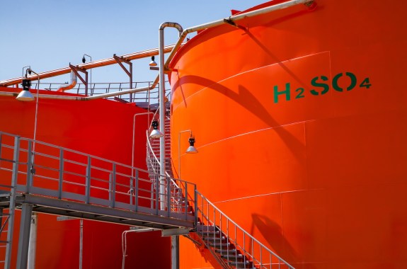 Orange metal storage tanks with sulfuric acid and its formula on tank.