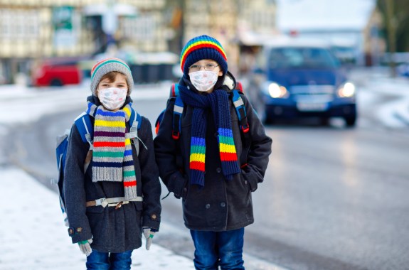 Two kids boys wearing medical mask on the way to school. Children with backpack satchel. Schoolkids on cold winter day with warm clothes. Lockdown and quarantine time during corona pandemic disease