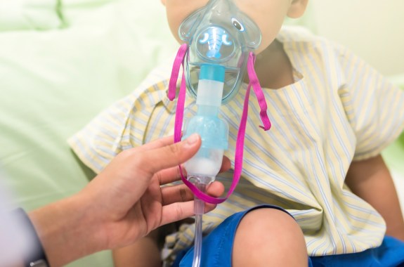 The lower third of a child's face is visible. Sick young boy, 3 years old, inhaling medication by inhalation mask to cure Respiratory Syncytial Virus (RSV) on hospital bed.