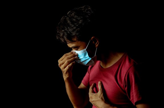 a man against a black background touching his face mask and putting a hand to his chest