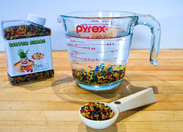 A tablespoon of multi-colored water beads have been added to two cups of water in a glass measuring Pyrex cup.
