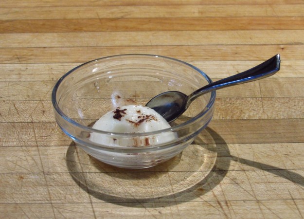 A small mound of opaque white ice cream in a clear glass bowl has melted and spread.