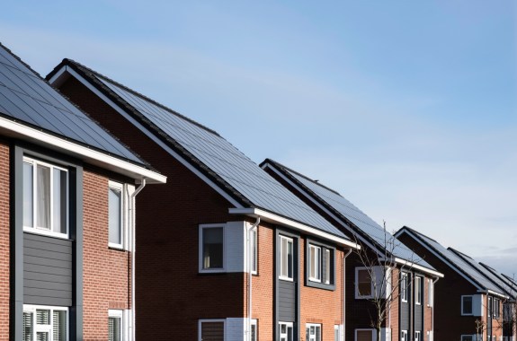 a row of four modern-looking simple two-story houses. each roof is covered in solar panels