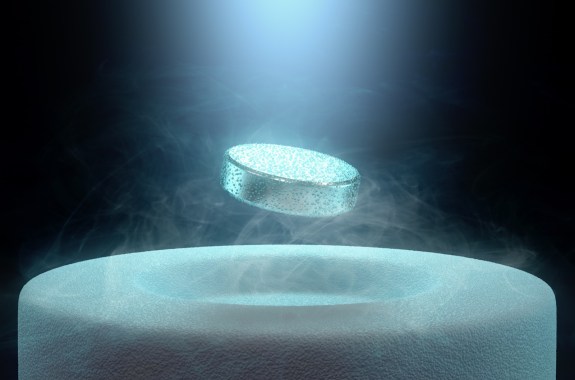 a metallic puck-shaped object floating above a white cylindrical object, with dust surrounding the puck. a light shines down from above, dramatically lighting the scene