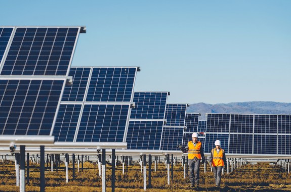 solar power station with two people in hard hats walking through many solar panels
