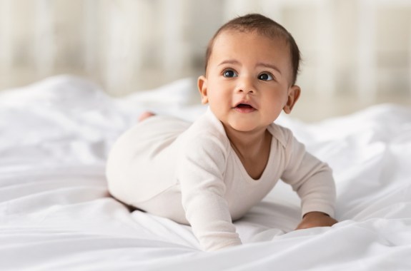 Childcare Concept. Portrait of cute baby wearing bodysuit lying on white beedsheets at home.