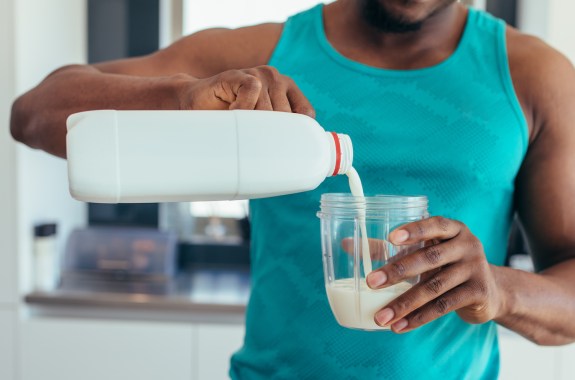 a black man in a blue tank pouring milk in a glass.