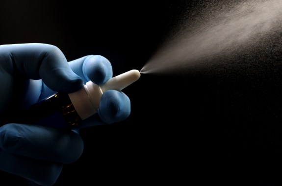 a hand squeezes a bottle of vaccine projecting mist spray, on a black background