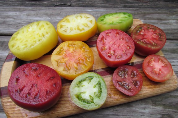 10 tomatoes sliced in half on a cutting board that are red, orange, yellow, and green.