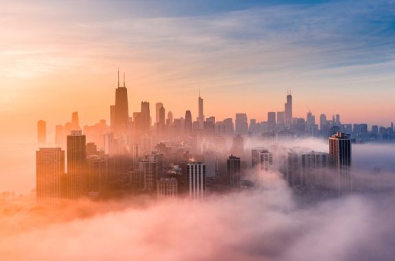 A photo of a foggy sunrise with Chicago skyline, shot from above the clouds from a drone