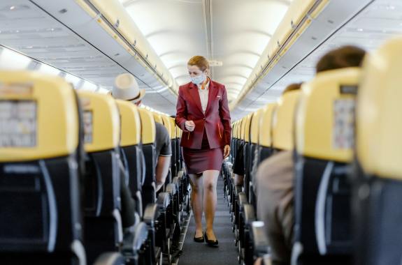 a flight attendant wearing a mask walks through a plane aisle