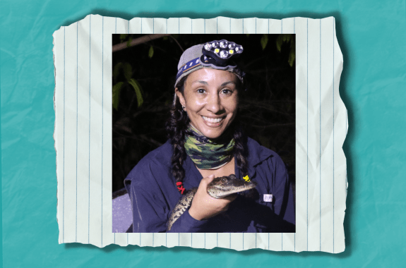 A woman holding a tiny crocodile with a headlamp on.