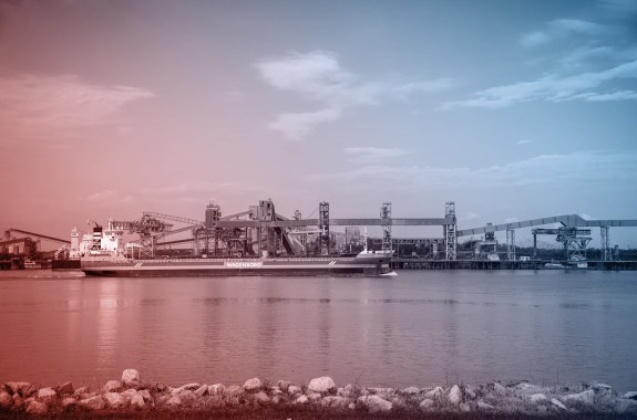 A red boat crosses a wide river on a sunny day